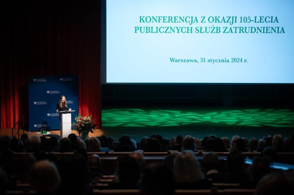 Zdjęcie przedstawiające scenę konferencji, na której znajduje się ministra rodziny, pracy i polityki społecznej.